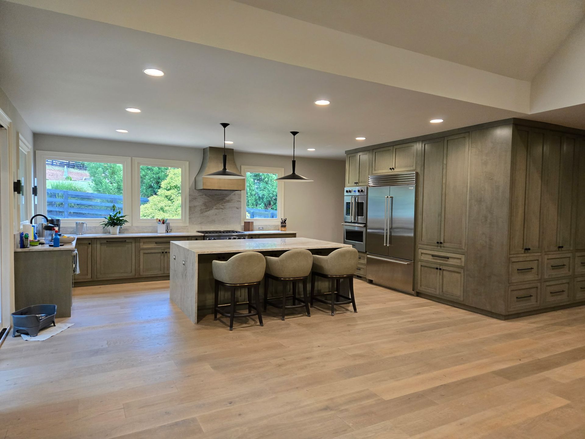Modern kitchen with island, pendant lights, gray cabinets, stainless appliances, and light wood floors