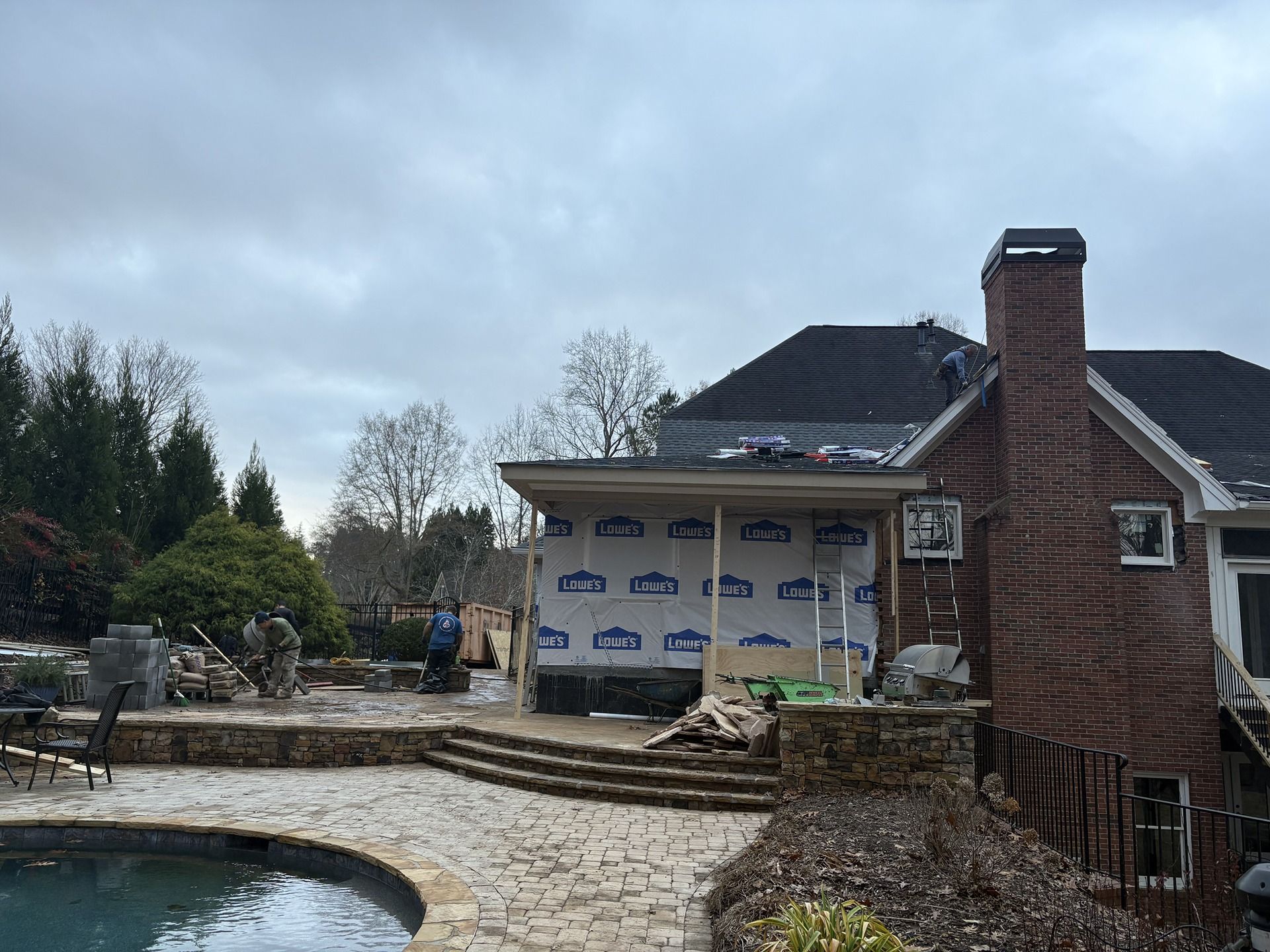 Backyard patio with a curved pool, stone steps, and a house under construction in the background