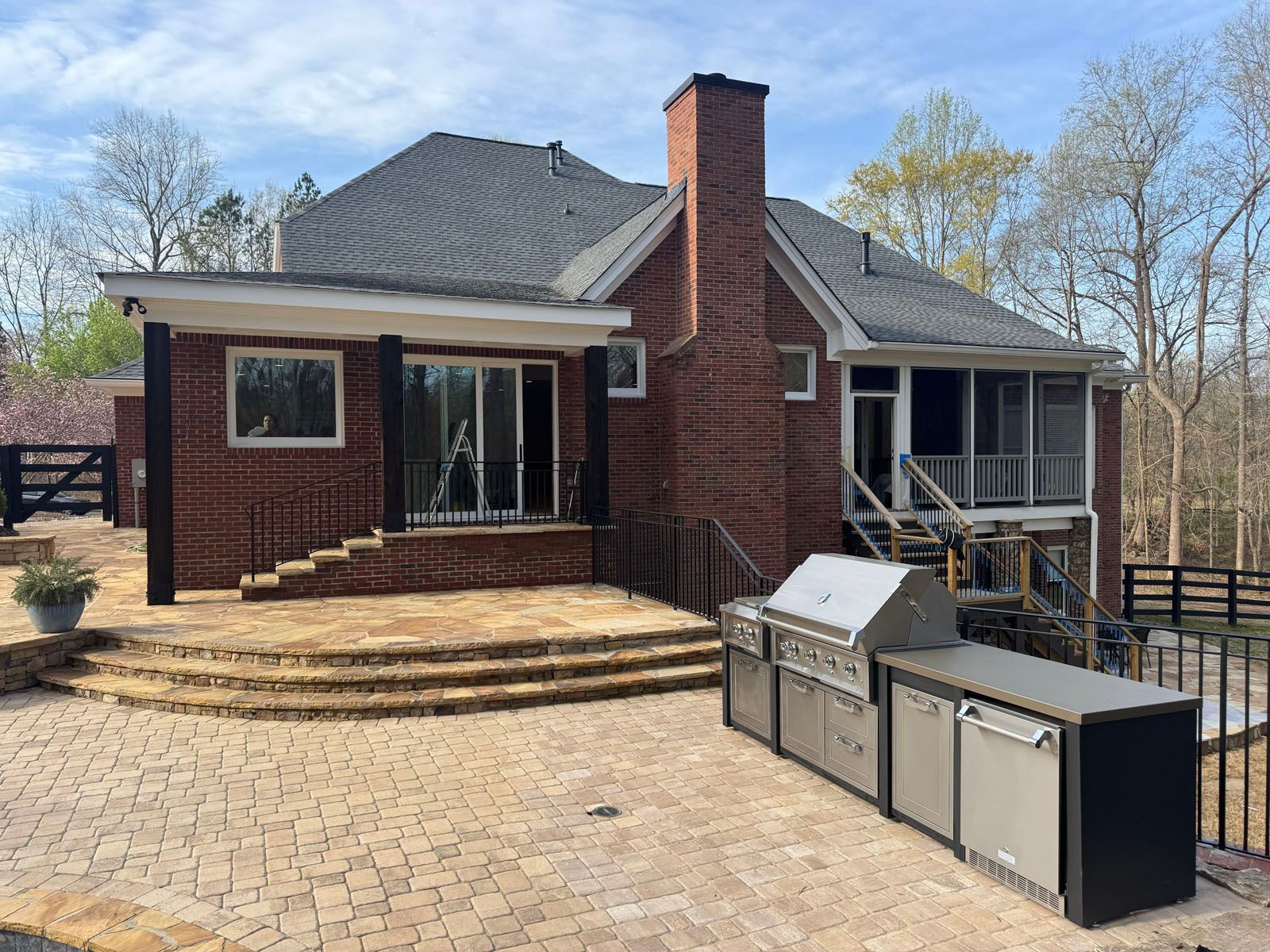 Brick house patio with curved steps, chimney, and outdoor kitchen on a sunny day