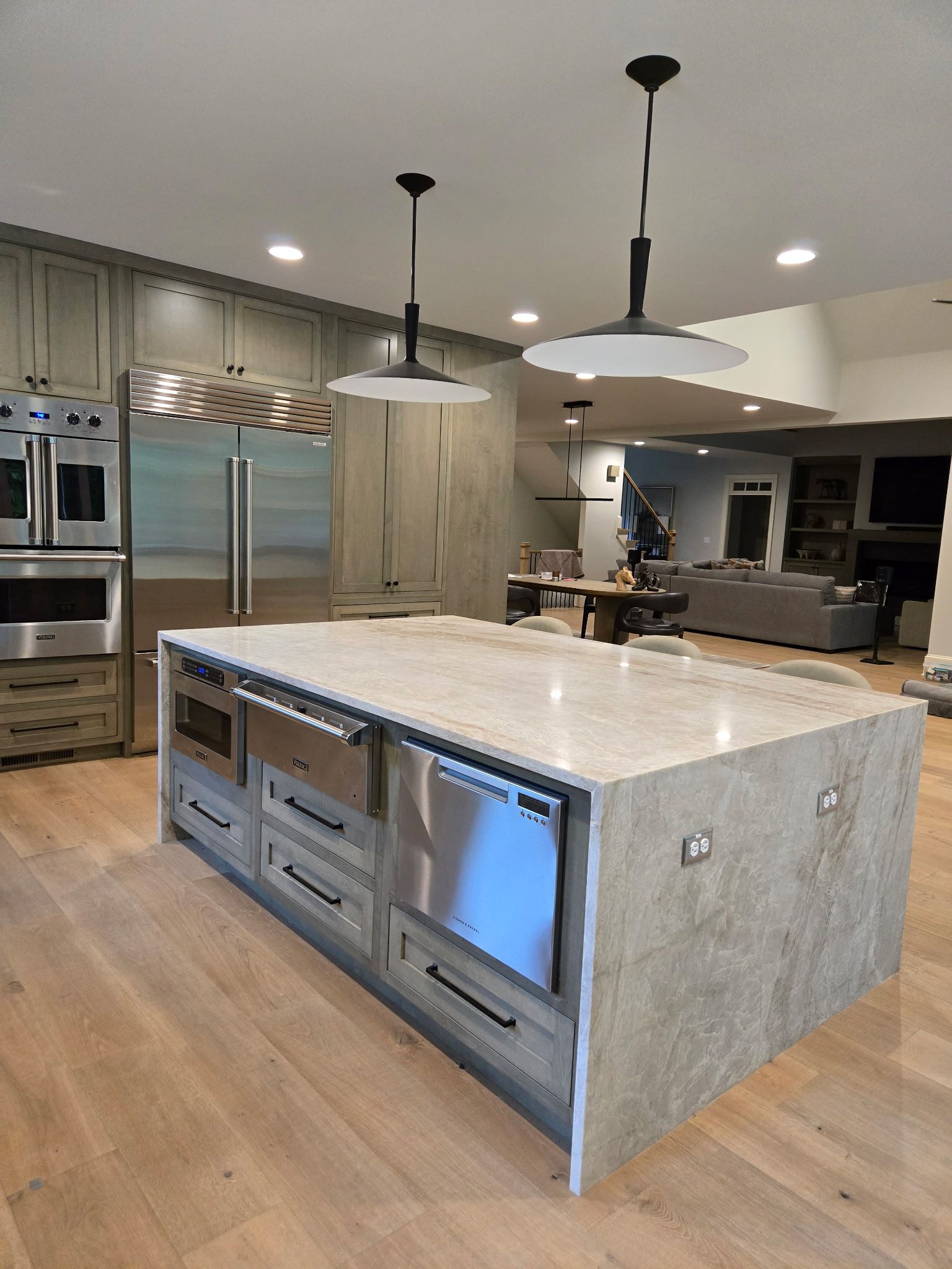 Modern kitchen with large stone island, stainless appliances, wood floors, and pendant lights