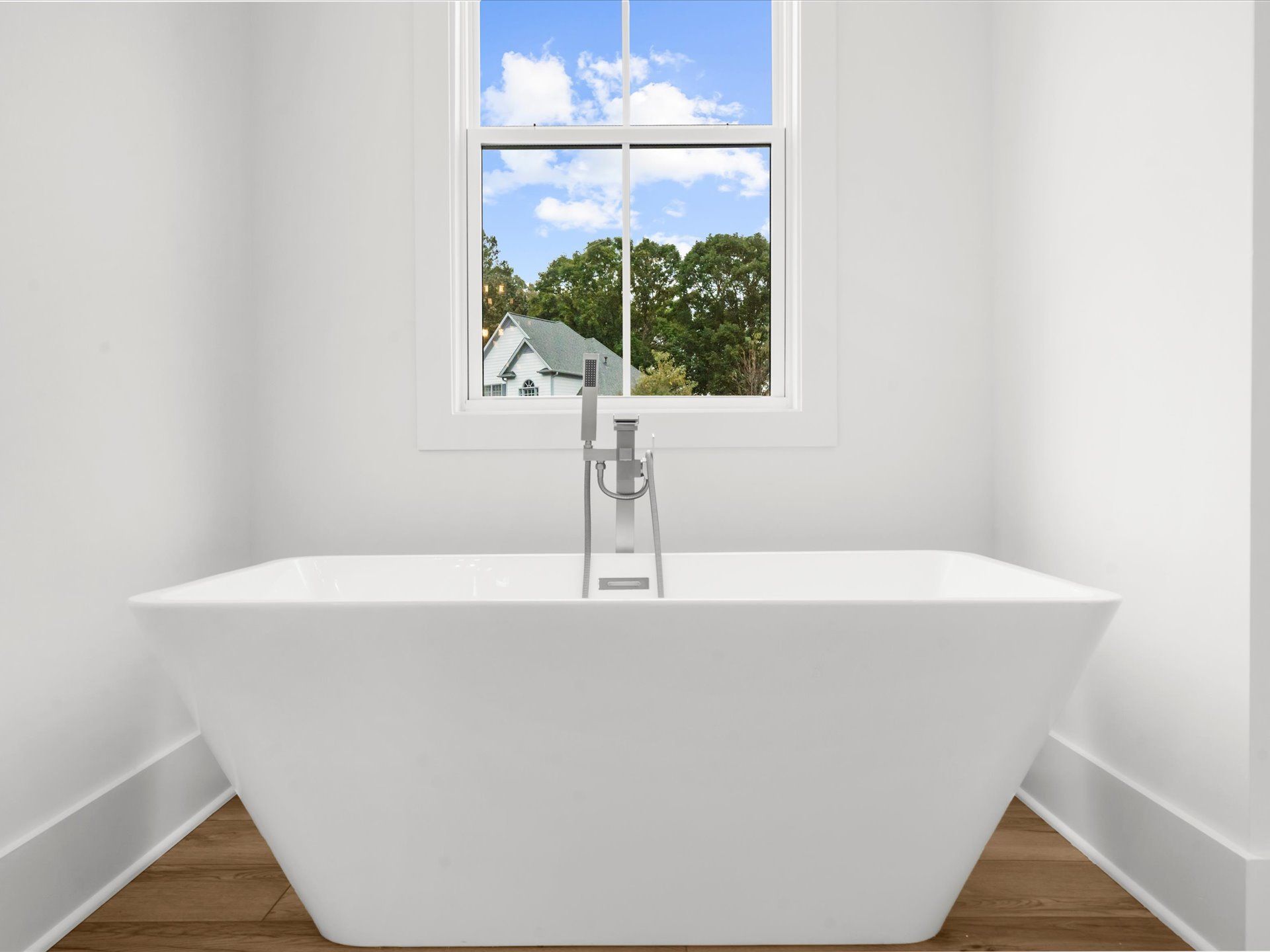 Minimalist white bathroom with freestanding tub centered under a window