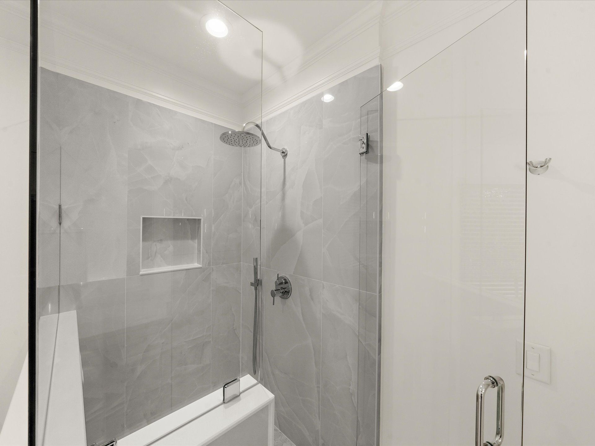 Modern gray-tiled bathroom shower with glass door and built-in shelf