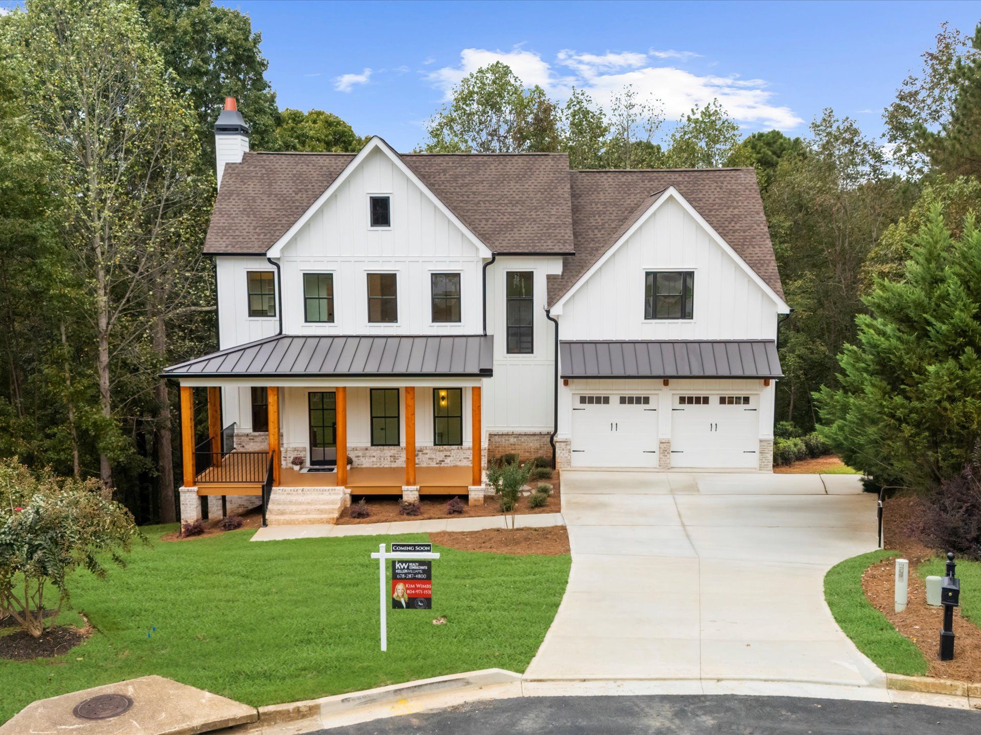 White two-story house with porch, detached garage, and long driveway in a wooded yard