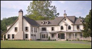 Large cream-colored suburban house with gabled roofs and a chimney, set behind a green lawn and trees