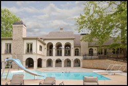 Luxury villa with arched balconies and a turquoise pool, surrounded by lounge chairs and trees