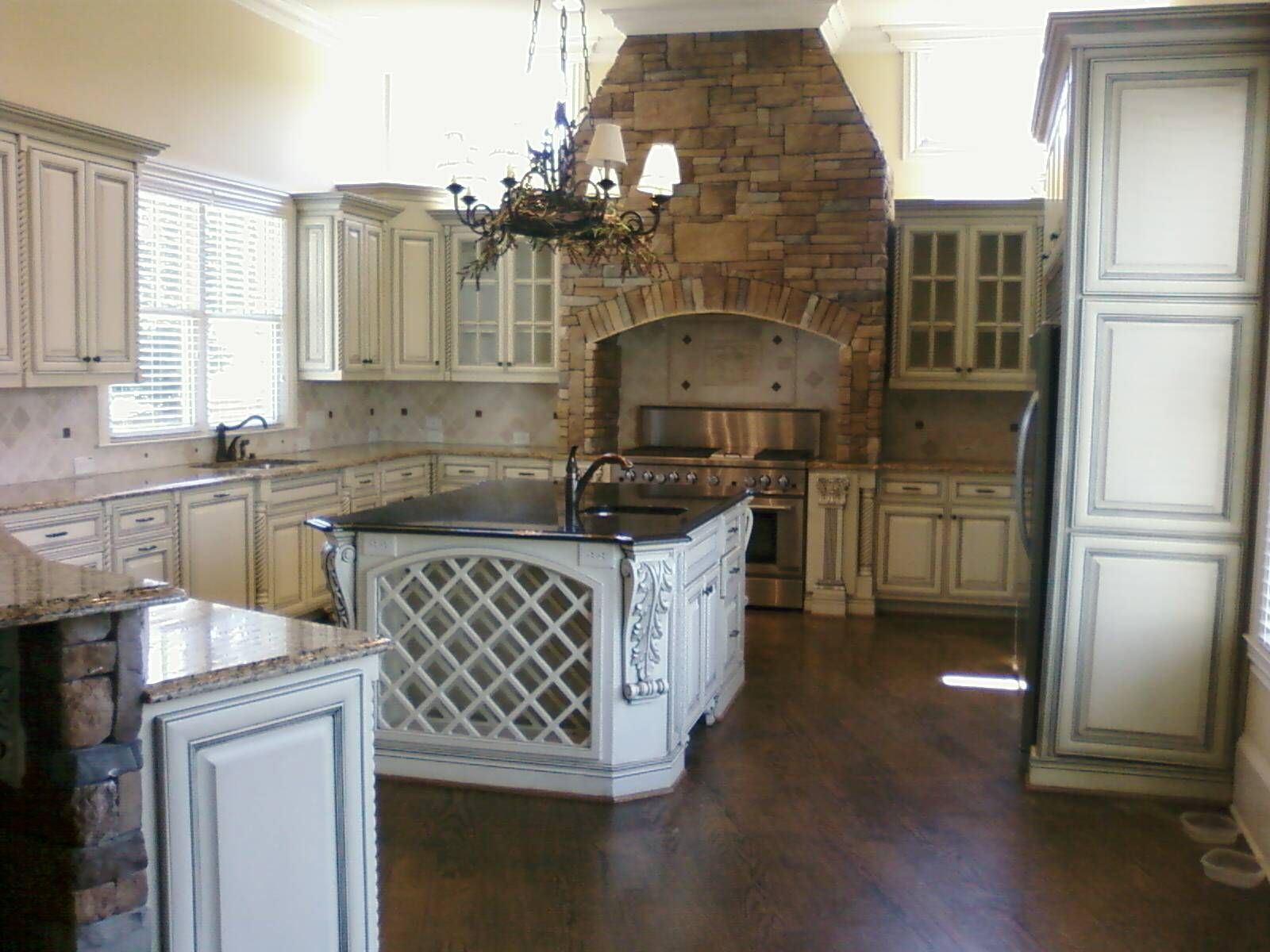 Spacious cream kitchen with a central island, wood floor, chandelier, and large stone range hood