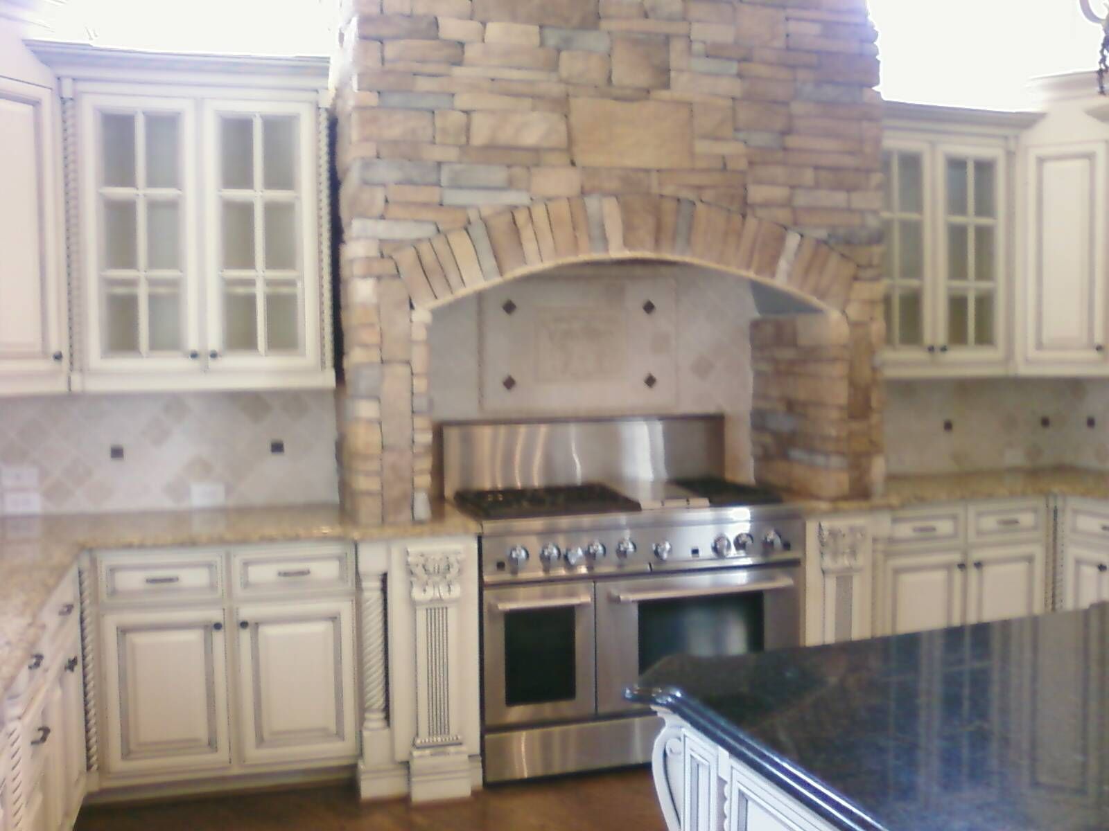 Elegant kitchen with stone range hood, stainless stove, cream cabinets, and dark granite island countertop