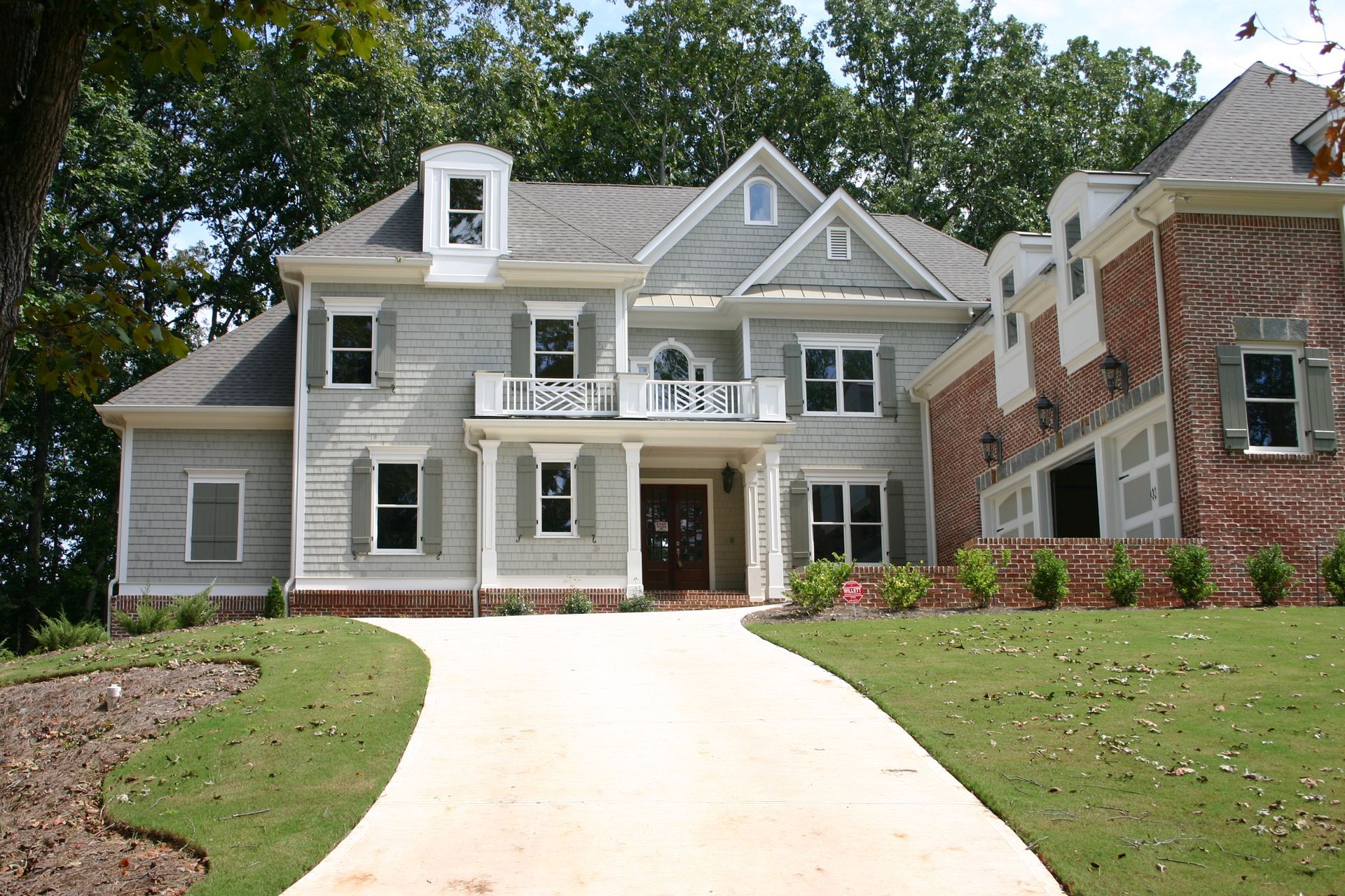 Large gray two-story house with a curved driveway and a brick home beside it