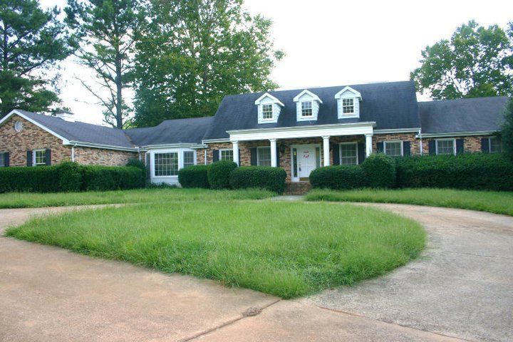 Suburban brick house with white columns, dormer windows, and a curved driveway in front.