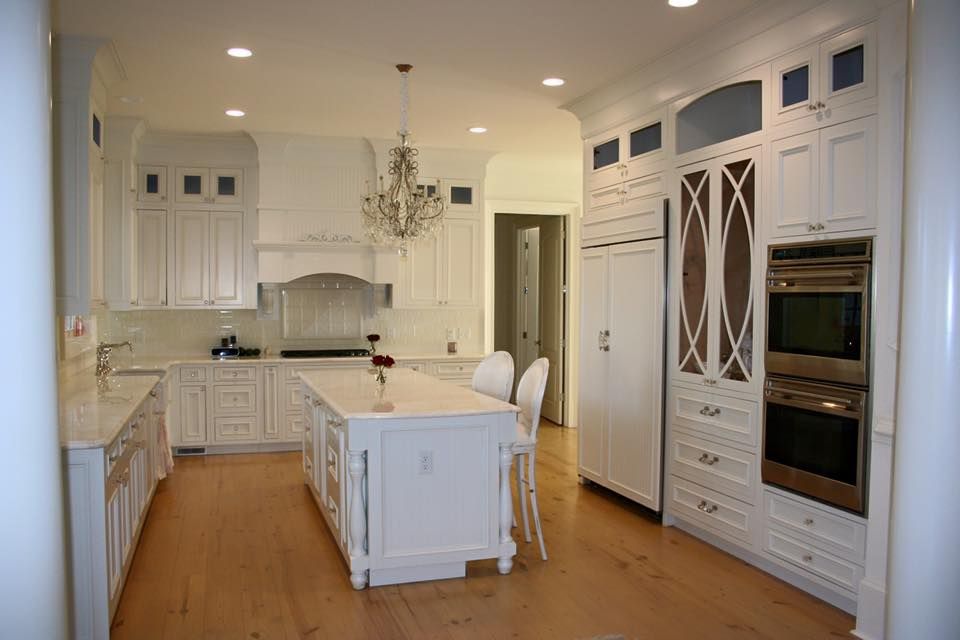 Bright white modern kitchen with island, wood floors, chandelier, and built-in ovens