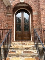 Brick building entrance with stone steps, black railings, and a wooden double door under an arched doorway