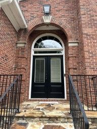 Brick entryway with black double doors, arched transom window, and stone steps with railings