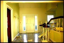 Bright yellow hallway with white front doors, patterned tile floor, and a staircase railing on the right