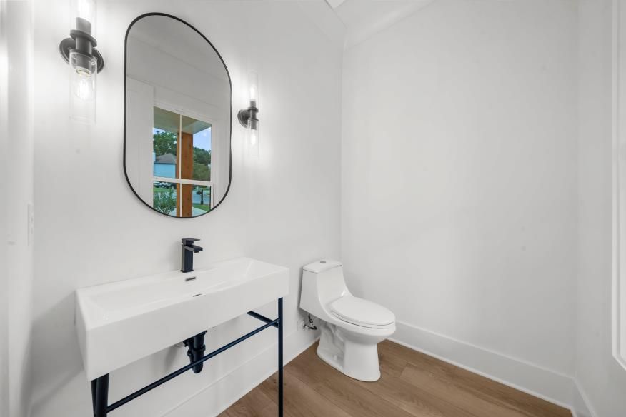 Minimal white bathroom with sink, oval mirror, toilet, and wood floor