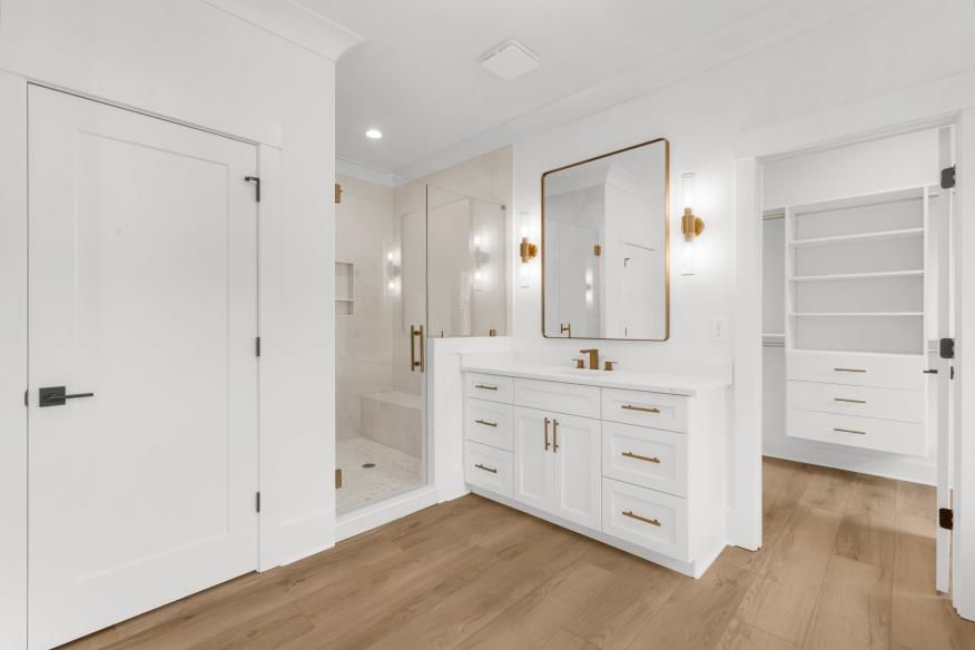 Bright modern bathroom with white vanity, gold mirror, and wood floor