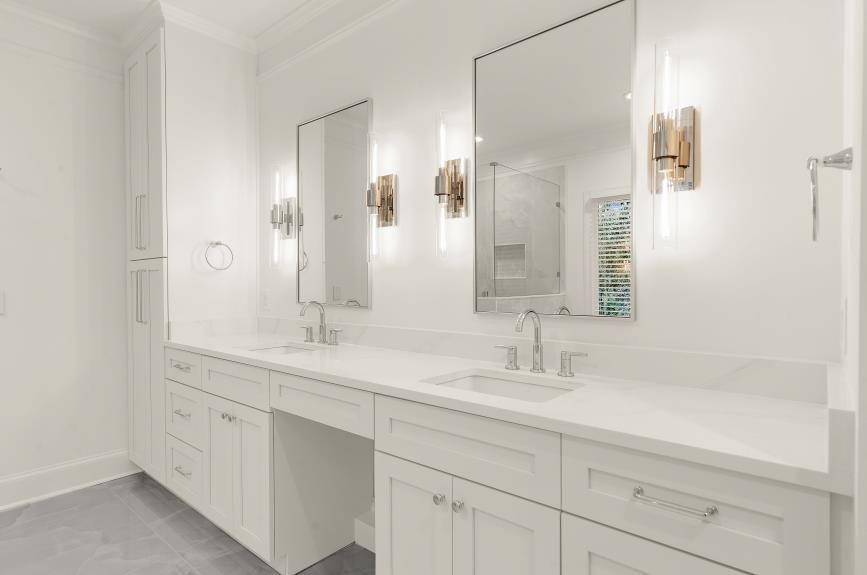 Bright white bathroom vanity with double mirrors, gold sconces, and built-in cabinets