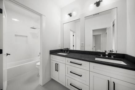 Modern white bathroom with double vanity, black countertop, large mirrors, and glass shower door