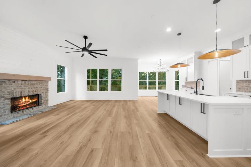 Bright open living room with fireplace, white kitchen island, and wide wood floors under modern pendant lights
