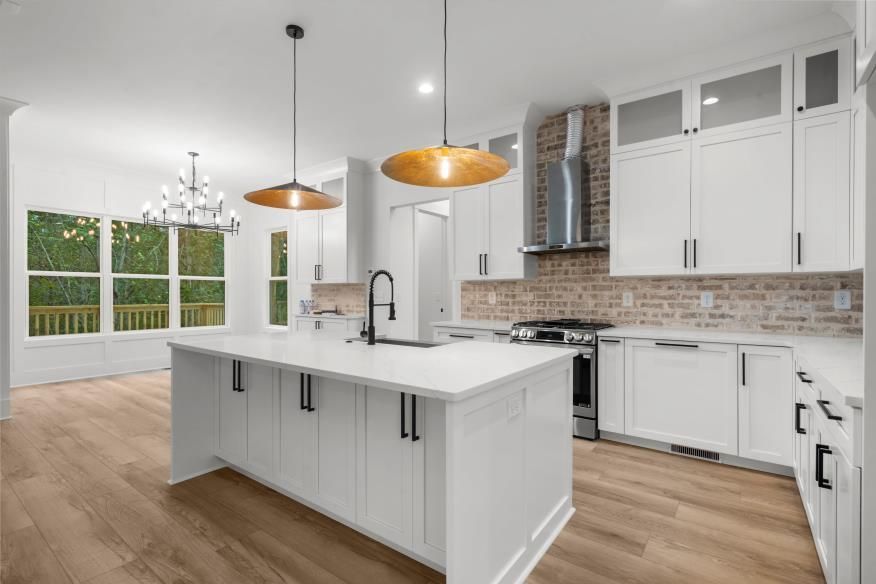 Bright modern kitchen with white island, wood floors, pendant lights, and large windows