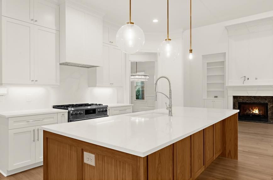 Bright white kitchen with wood island, pendant lights, and a lit fireplace in the background