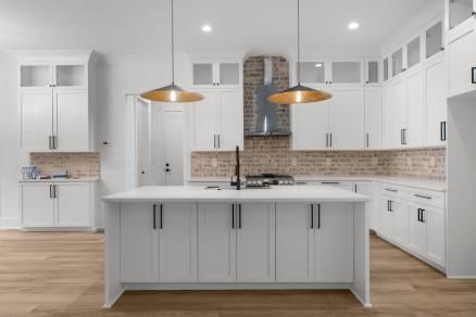 Bright white kitchen with central island, wood floors, pendant lights, and stainless steel appliances