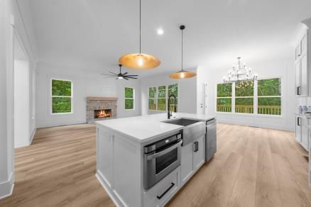 Bright open kitchen with white cabinets, wood floors, island, and large windows beside a fireplace