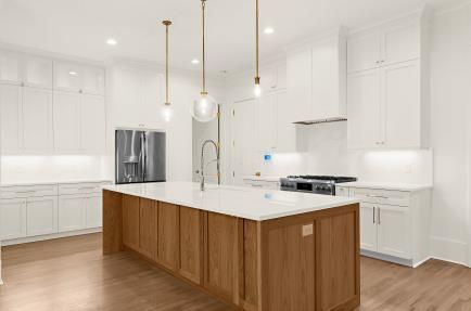 Bright white modern kitchen with a large wood island, stainless appliances, and pendant lights.