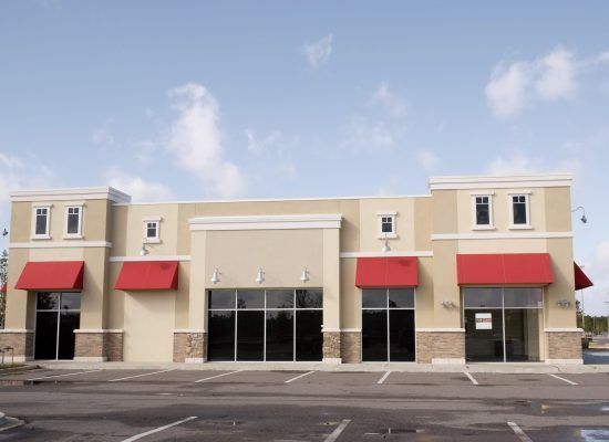 Strip mall storefront with red awnings and a central glass entrance under a blue sky