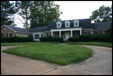 Suburban house with a dark roof, white columns, and a curved driveway in front of a green lawn.