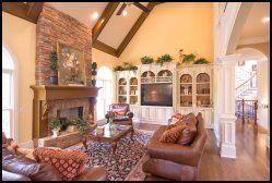 Spacious living room with brick fireplace, leather sofas, floral rug, and built-in white cabinets under vaulted ceiling