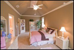 Bright bedroom with beige walls, a large bed, white nightstands, and a ceiling fan; open doorway and mirror visible.