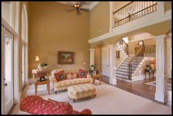 Spacious living room with high ceilings, staircase, beige walls, and red-patterned sofas