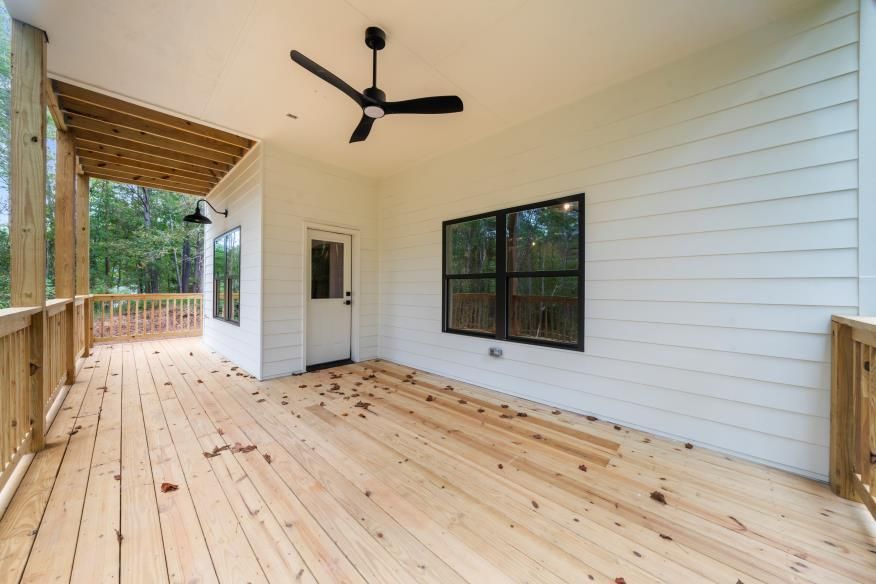 Covered wooden porch with white siding, black ceiling fan, and large windows overlooking trees.