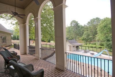 Covered patio overlooking a backyard pool and trees, with wicker chairs and arched columns