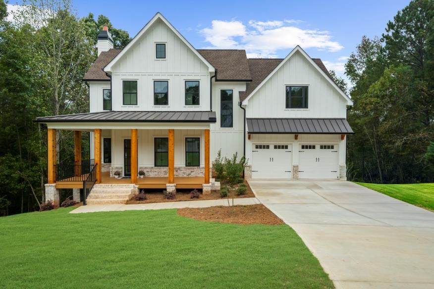 Two-story white house with a front porch, attached garage, and green lawn on a sunny day
