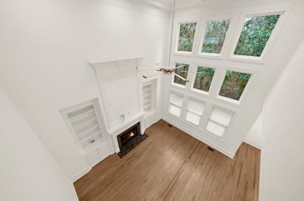Bright empty living room with fireplace, white walls, wood floor, and large windows