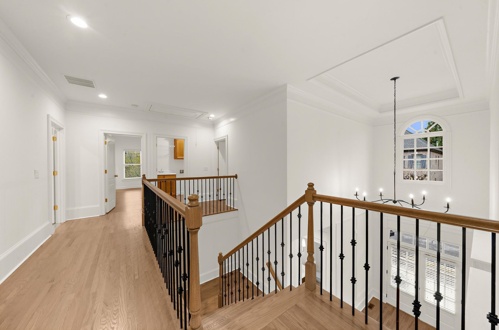 Bright hallway with wood floors and stair railing overlooking a sunlit entryway