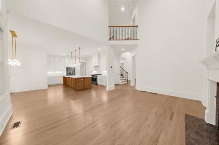 Bright open-plan living room with light wood floors, white walls, kitchen island, and staircase.