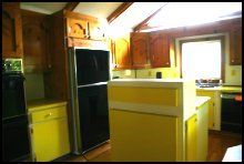Bright kitchen with yellow cabinets, black refrigerator, and sunlight through a window.