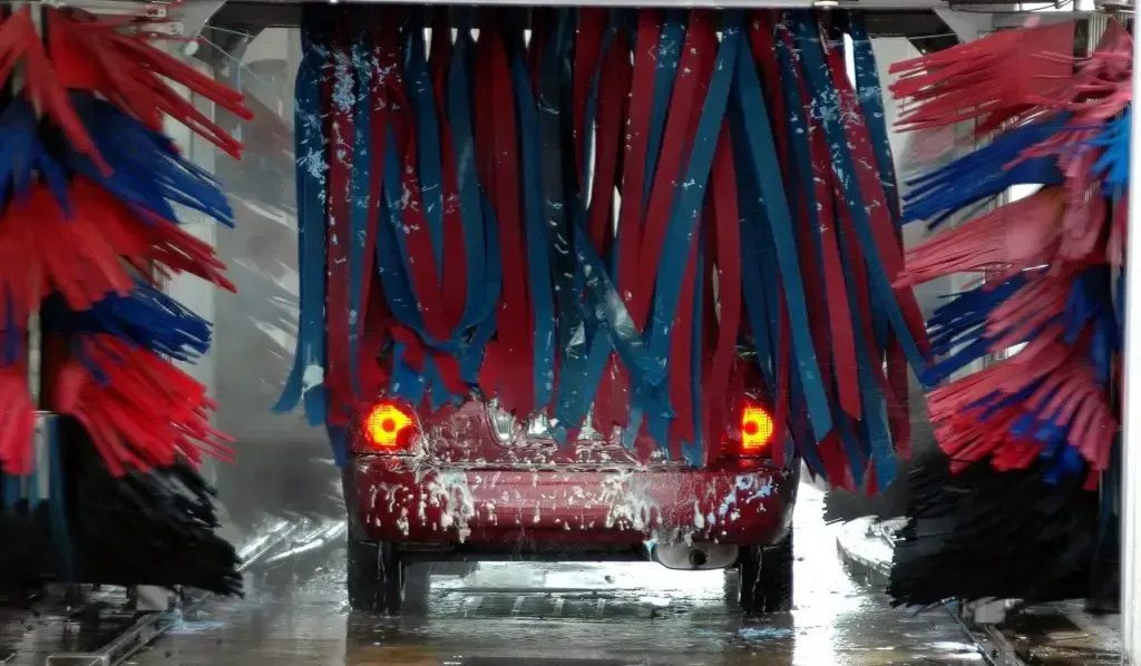 A car is going through a car wash with red and blue brushes.