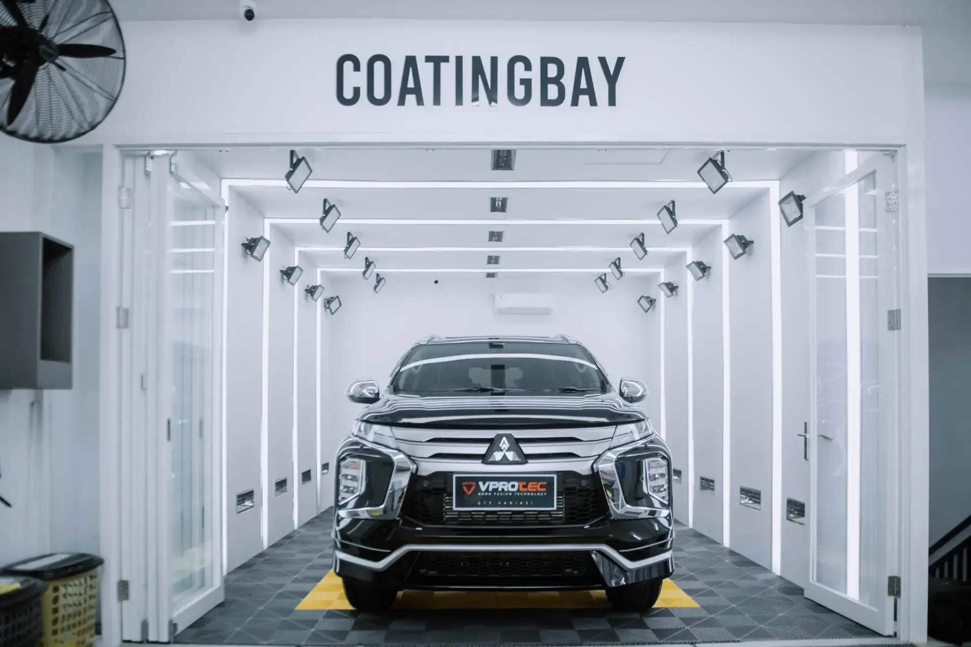 A black car is parked in a coating bay.