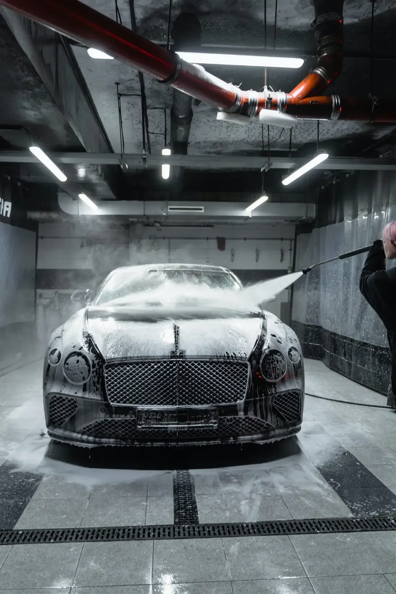 A woman is washing a bentley in a car wash.