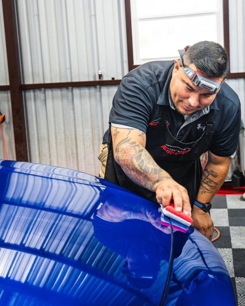 A man is polishing a blue car in a garage.