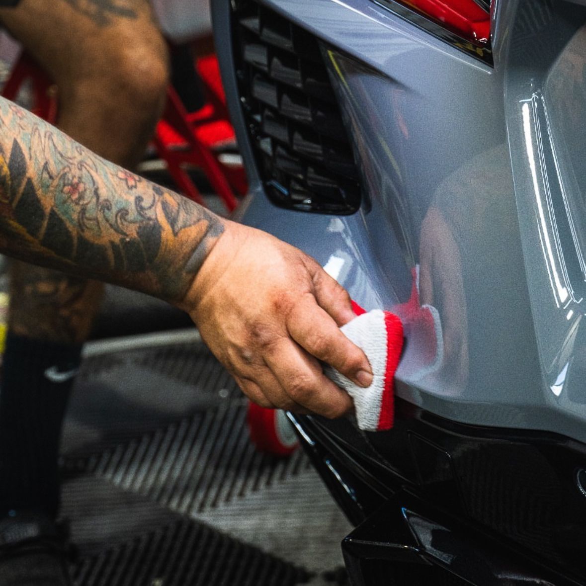 A man with a tattoo on his arm is cleaning a car with a sponge