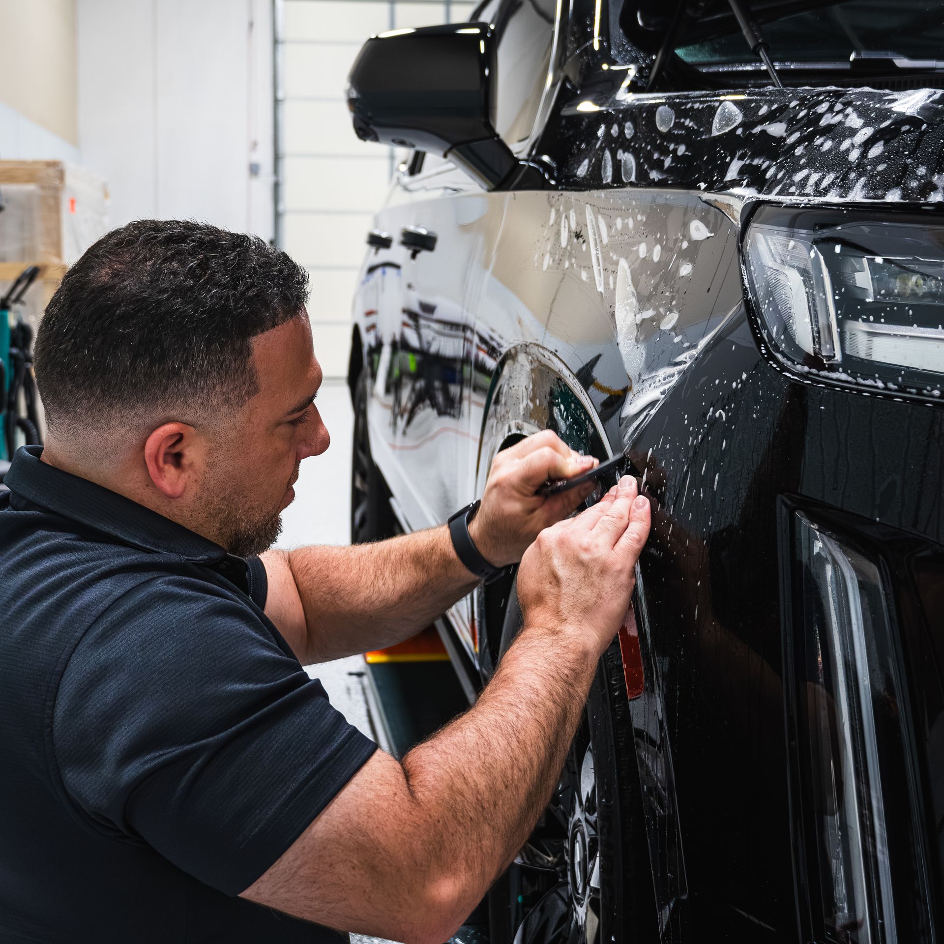 A man is working on a black car in a garage.