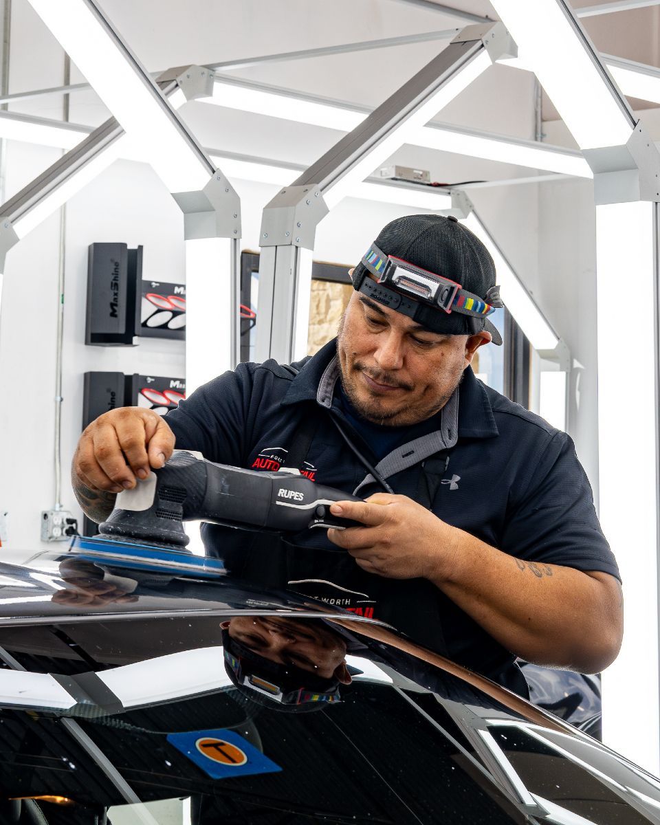 A man is polishing a car with a machine in a garage.