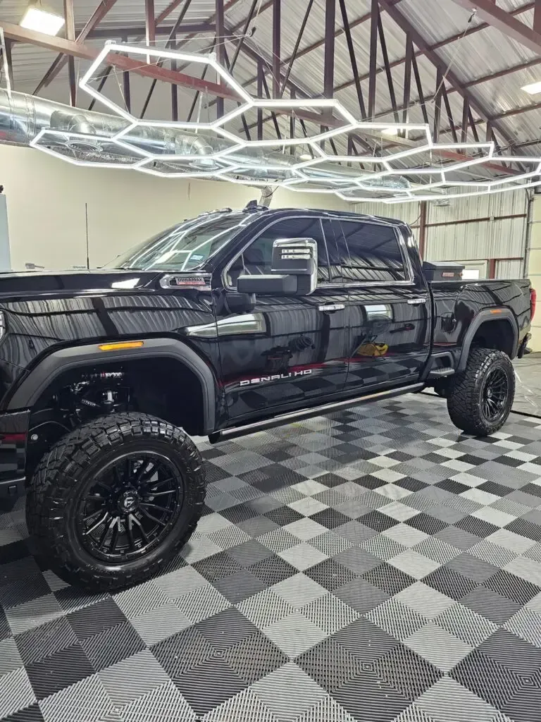 A black truck is parked in a garage with a checkered floor.