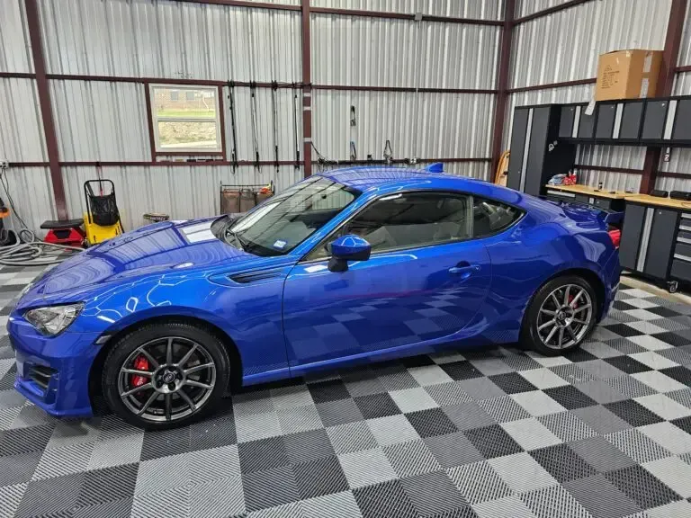 A blue sports car is parked in a garage with a checkered floor.