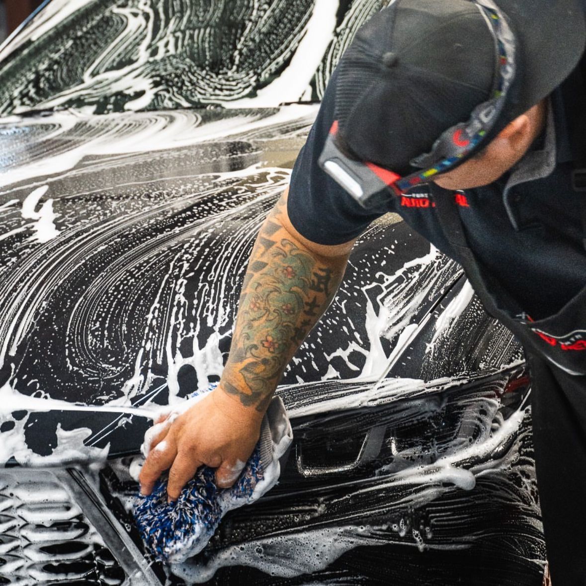 A man with a tattoo on his arm is washing a car