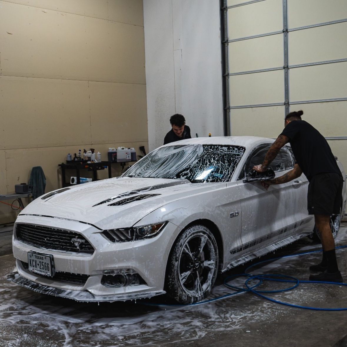 A man is washing a white mustang in a garage.